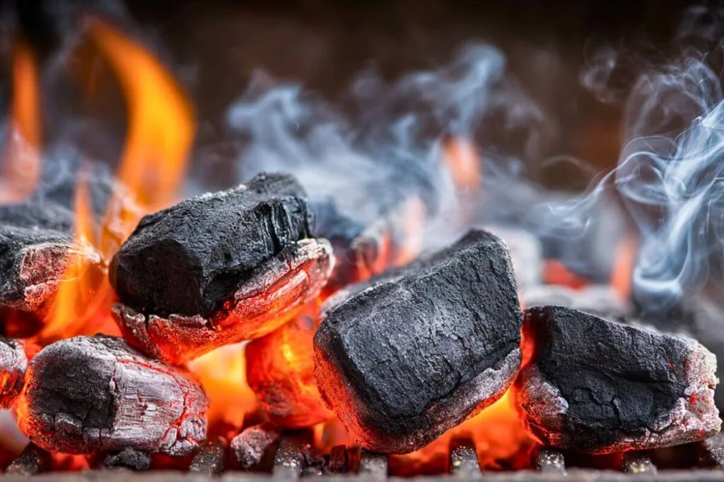 Close-up of burning charcoal briquettes with glowing embers and smoke rising – ideal for illustrating the topic 'Does Charcoal Go Bad' and how to tell if charcoal is still good for grilling.